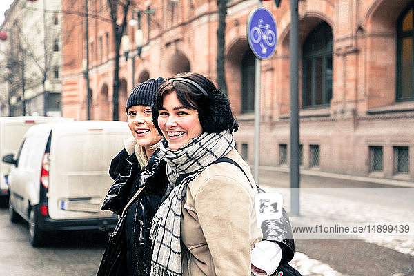 Porträt fröhlicher junger Frauen in warmer Kleidung  die im Winter in der Stadt auf der Straße stehen