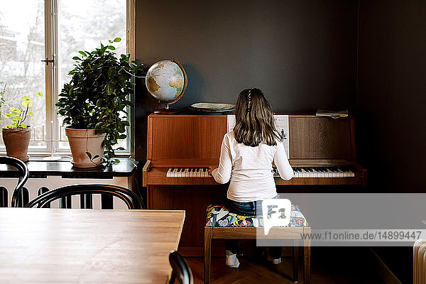 Rückansicht eines Mädchens  das Klavier spielt  während es zu Hause im Wohnzimmer sitzt