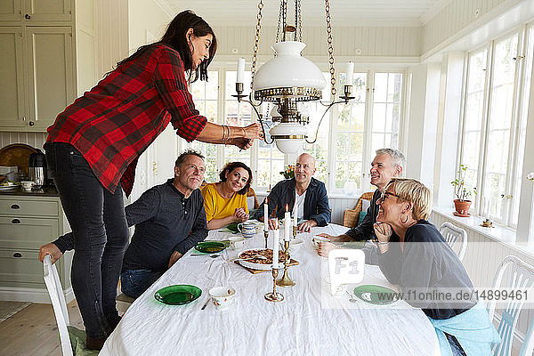 Freunde schauen Frau an  die zu Hause Essen auf dem Esstisch fotografiert
