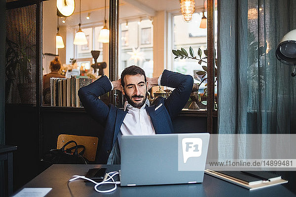 Businessman with hands behind head looking at laptop on desk in creative office