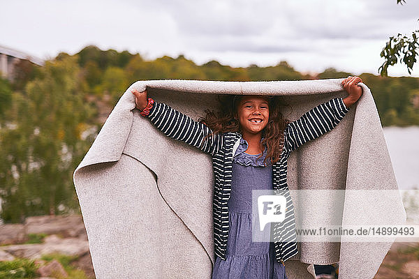 Portrait of cheerful girl holding blanket while standing in park during picnic