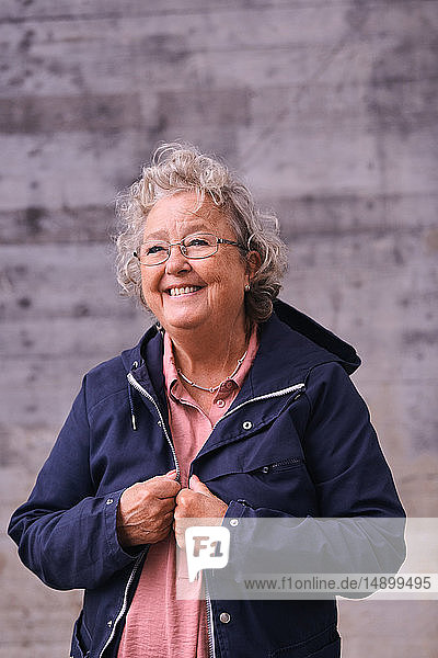 Fröhliche ältere Frau im Regenmantel mit Blick nach draußen
