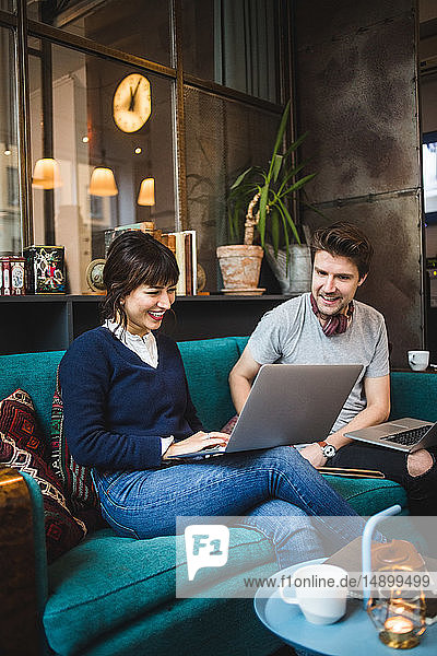 Smiling multi-ethnic male and female entrepreneurs discussing over laptop on sofa at office