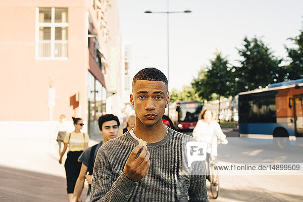 Portrait of teenage boy holding food while walking on street in city