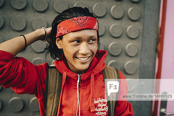 Fröhlicher junger Mann mit rotem Halstuch beim Wegschauen in der Stadt