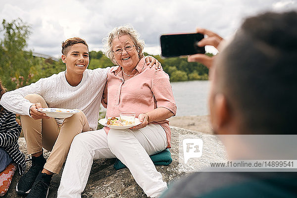 Mann fotografiert Enkel und Großmutter beim Picknick mit Mahlzeit auf Fels