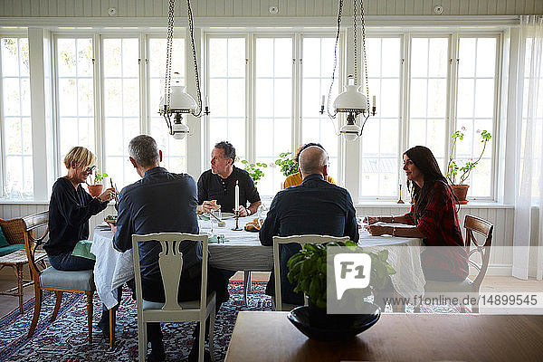 Mature friends having meal while sitting in dining room at home
