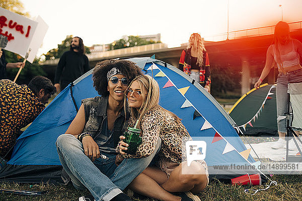 Portrait of smiling friends sitting outside tent on lawn at musical event