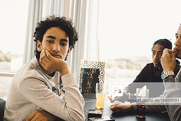 Portrait of serious teenage boy sitting with friends at table in restaurant