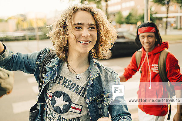 Lächelnder junger Mann schaut weg  während ein Freund im Hintergrund auf der Straße steht