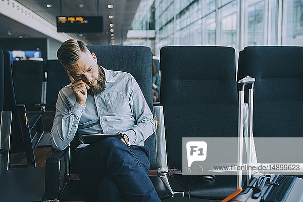 Geschäftsmann benutzt digitales Tablet  während er im Wartezimmer im Abflugbereich des Flughafens sitzt