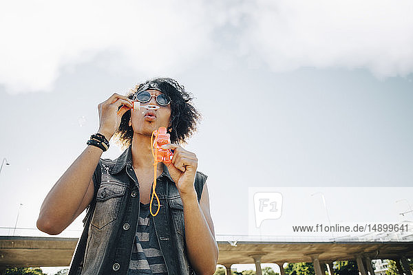 Low angle view of young man blowing soap bubbles against sky
