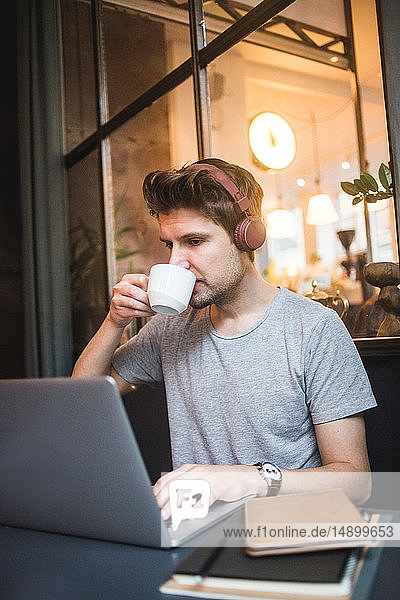 Confident businessman drinking coffee while using laptop at desk in office