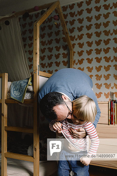 Vater küsst Tochter  während er sie zu Hause im Schlafzimmer anzieht