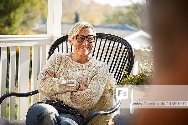 Cheerful mature woman with arms crossed looking away while sitting on porch