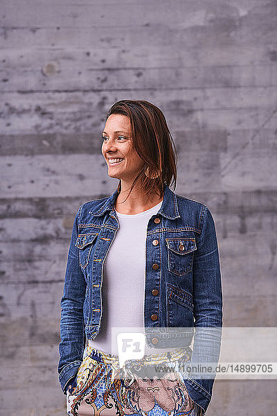 Cheerful mature woman with hands in pockets looking away while standing outdoors