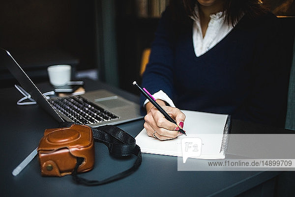 Midsection of businesswoman writing in diary at desk