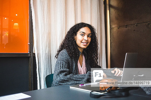 Porträt einer lächelnden Jungunternehmerin  die mit Laptop am Schreibtisch im Büro sitzt