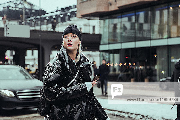 Junge Frau trägt warme Kleidung  während sie im Winter auf der Straße in der Stadt wegschaut