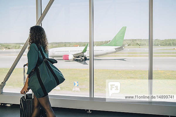 Geschäftsfrau geht mit Gepäck am Fenster im Korridor des Flughafens
