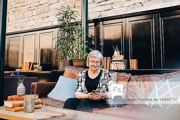 Ältere weibliche Touristin benutzt Smartphone  während sie im Restaurant auf dem Sofa sitzt