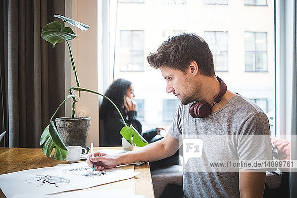 Selbstbewusster männlicher Grafikdesigner  der auf Papier bei Tisch im Büro zeichnet