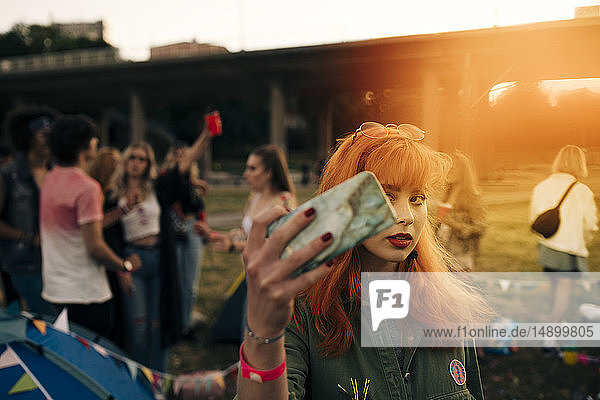 Redhead young woman taking selfie on smart phone with friends in background