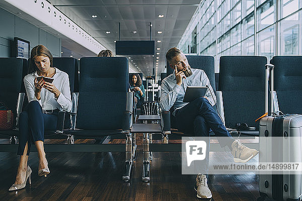 Thoughtful businessman looking away while sitting by female colleague at waiting area in airport
