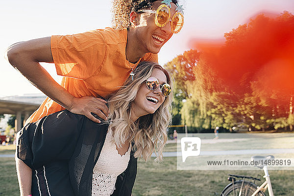 Happy young woman piggybacking man wearing novelty glasses