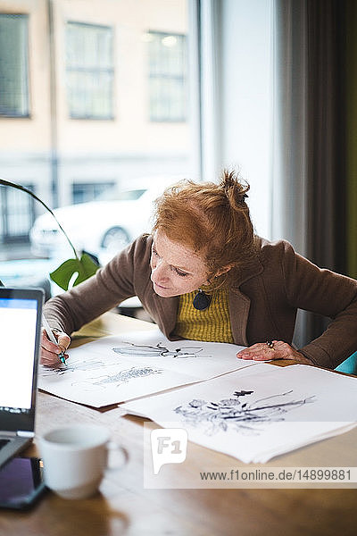 Selbstbewusste weibliche Illustratorin zeichnet auf Papier bei Tisch im Büro