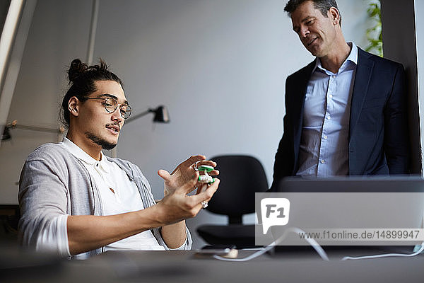 Männlicher Unternehmer diskutiert mit Bankmanager über Solarspielzeugauto im Kreativbüro
