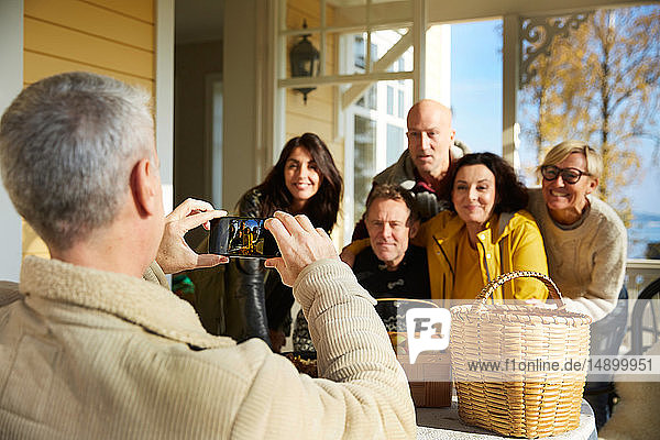 Mature man photographing friends with smart phone on porch