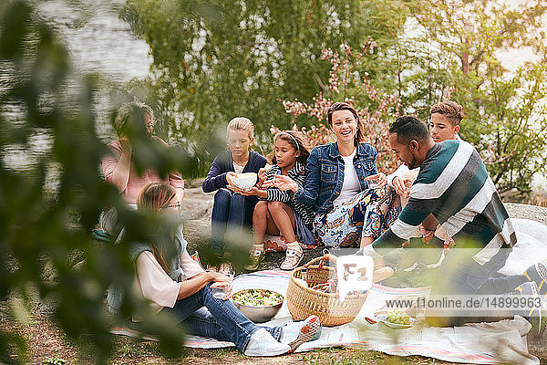 Happy family and friends having food on lakeshore in park