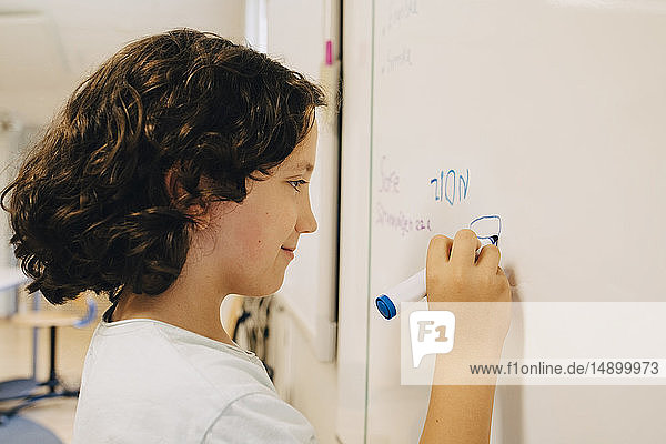 Side view of boy with curly hair writing on whiteboard at classroom