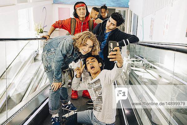 Glückliche männliche Freunde  die sich mit einem Smartphone auf dem Laufsteg eines Einkaufszentrums selbstständig machen