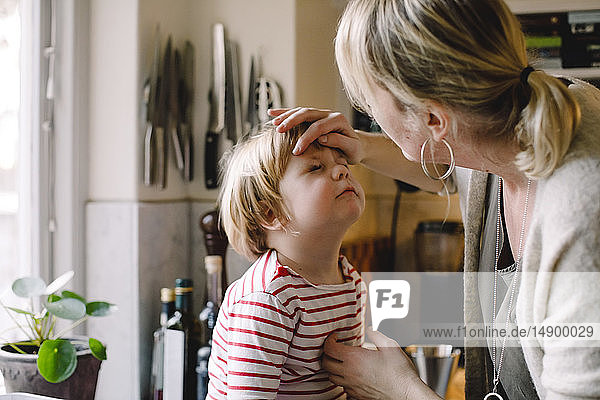 Pflegende Mutter schaut auf das geprellte Auge ihrer Tochter in der Küche