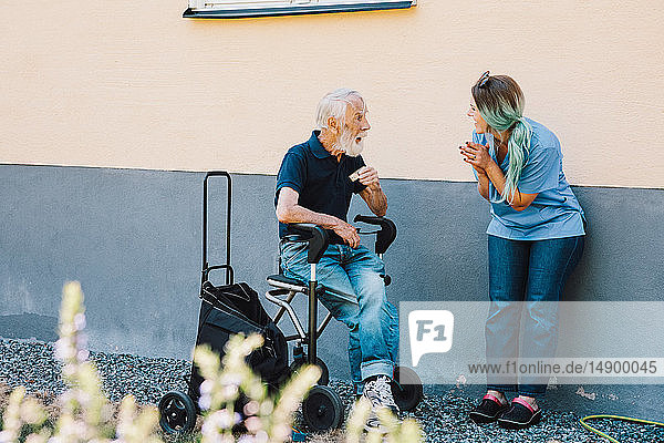 Lächelnde Krankenschwester klatscht beim Anblick eines älteren Mannes  der im Rollstuhl an der Wand im Hinterhof sitzt