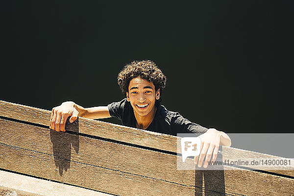 Hochwinkelporträt eines fröhlichen Teenagers  der am Pier am Fluss hängt