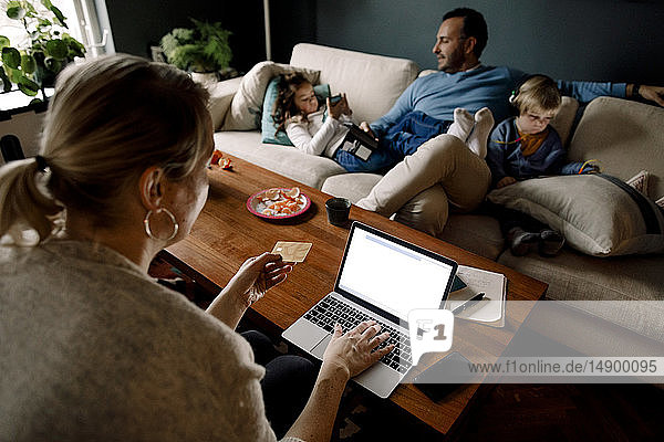 Mutter online einkaufen  während Mann und Töchter verschiedene Technologien im Wohnzimmer nutzen