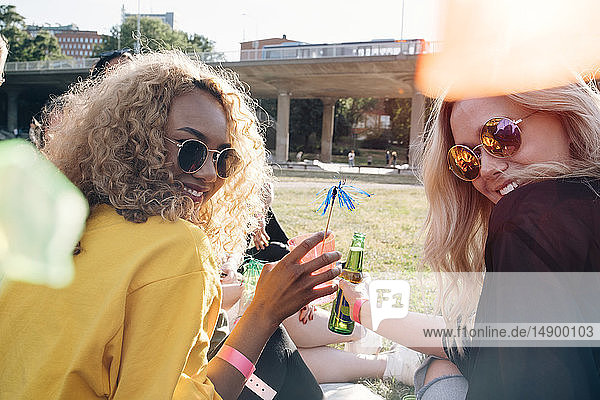 Lächelnde Freunde genießen Getränke  während sie beim Konzert auf dem Rasen sitzen