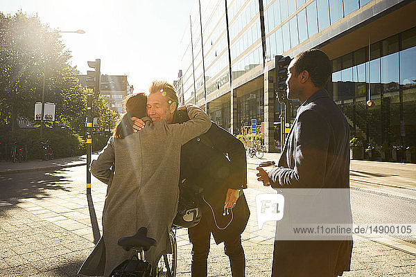 Junger Mann sieht Freunde an  die sich auf dem Bürgersteig in der Stadt umarmen