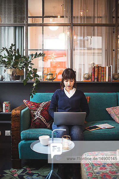 Selbstbewusste weibliche Fachkraft in voller Länge mit Laptop auf dem Bürosofa sitzend