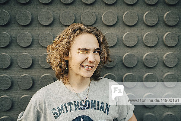 Porträt eines lächelnden jungen Mannes  der mit einem Augenzwinkern an die Wand winkt