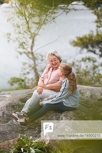 Grandmother and granddaughter talking while sitting on rock in park