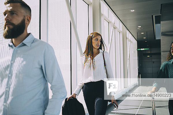 Junge Geschäftsfrau unterhält sich mit einer Kollegin  während sie im Korridor des Flughafens geht