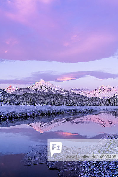 Alpenglow colours the snow-covered coastal range mountains Mendenhall Glacier and Mendenhall towers are reflected in the open water along the edge of Auke Lake as the sun gets ready to set; Alaska United States of America