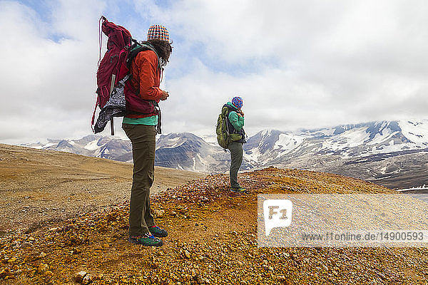 Two women backpacking and taking in the view of Mount Katmai from the rainbow-coloured pumice  rock and clay slopes of Broken Mountain  Valley of Ten Thousand Smokes  Southwest Alaska; Alaska  United States of America