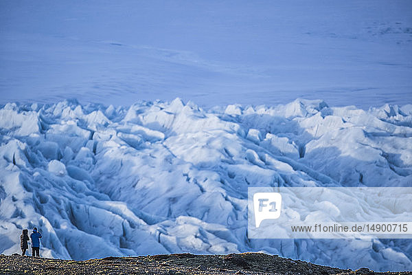 Zwei Personen beim Wandern und Fotografieren eines Gletschers an der Südküste Islands; Island