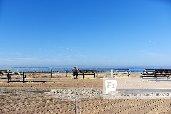 Man sitting on bench along Coney Island boardwalk looking out to the Atlantic Ocean; New York City  New York  United States of America