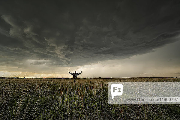 Dramatischer Himmel über der Landschaft während einer Sturmjagd im Mittleren Westen der Vereinigten Staaten. Mann steht auf dem Feld und beobachtet den herannahenden Sturm; Kansas  Vereinigte Staaten von Amerika